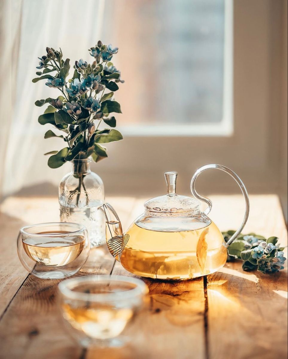 Hot water being poured from a kettle over loose herbs in a clear glass teapot